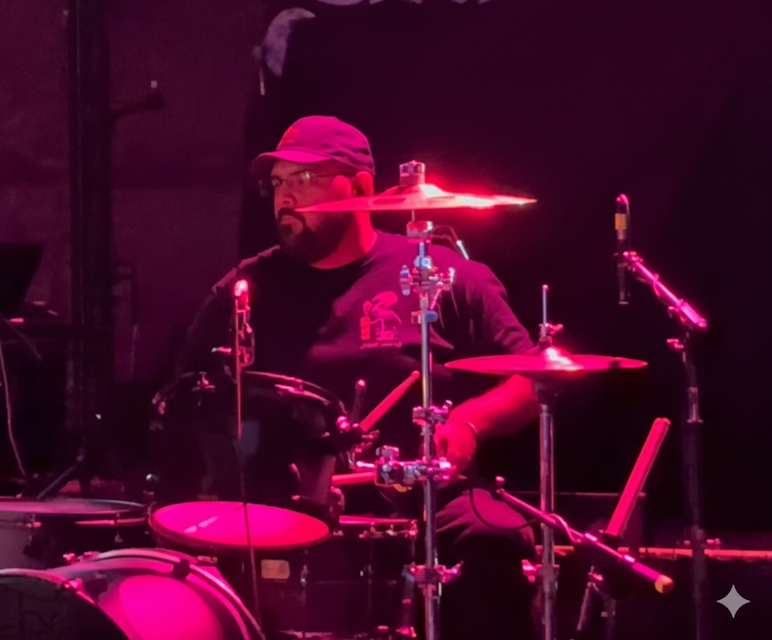 Second Illusion drummer performing live on stage under red lighting, focused mid-performance behind the drum kit at BFE Rock Club.